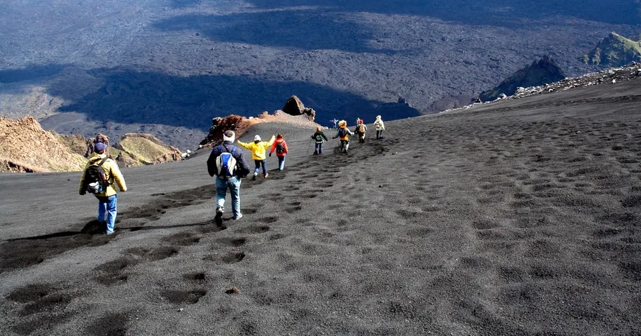 A line of hikers walking up black volcanic sand towards the summit cone of Etna